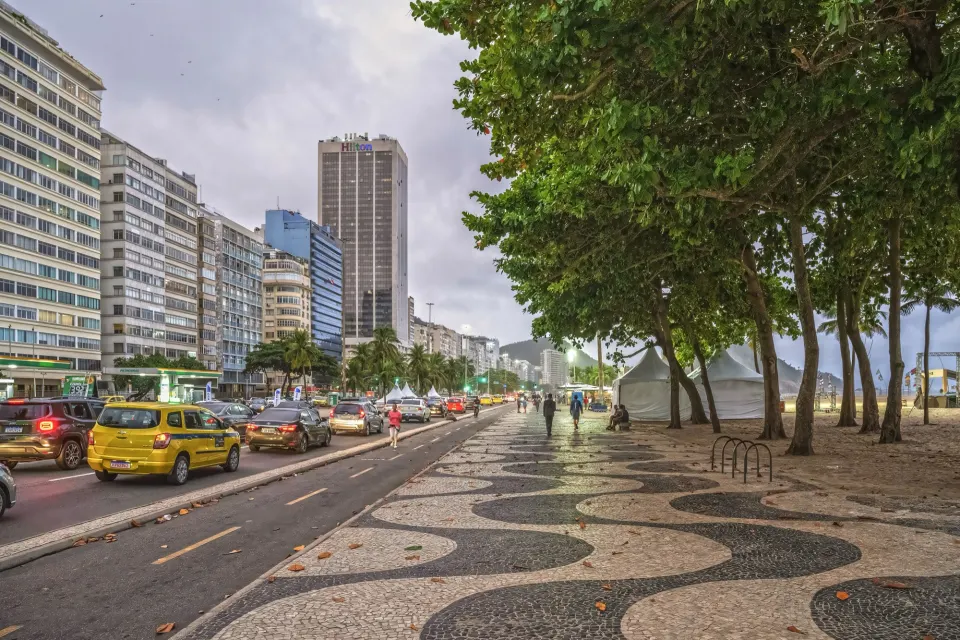 Cars and a yellow taxi on Avenida Atlântica beside Copacabana's wave-pattern promenade