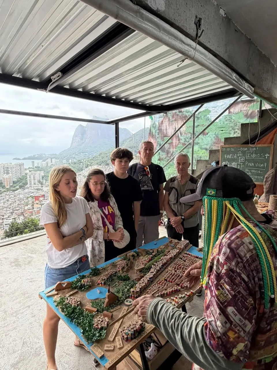 A local guide explains a handmade model of the favela to a group of travellers