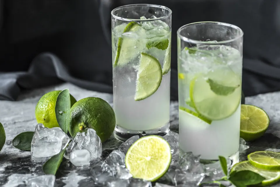 Two glasses of caipirinha-style lime drinks with ice cubes and fresh limes
