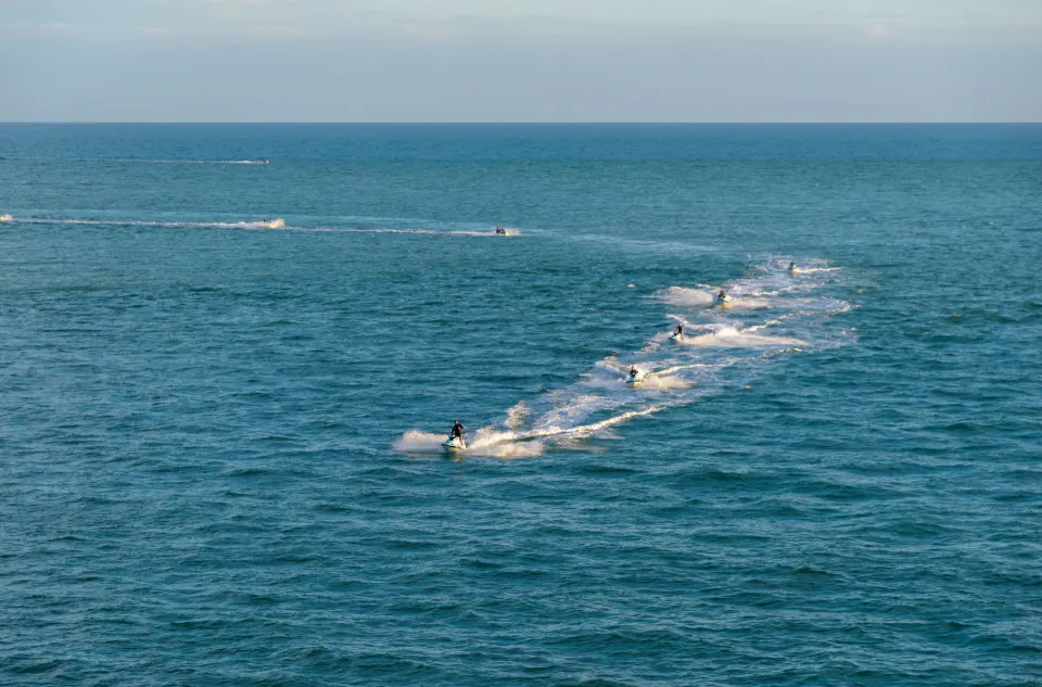 Group of jet ski riders leaving white wakes across open blue sea water