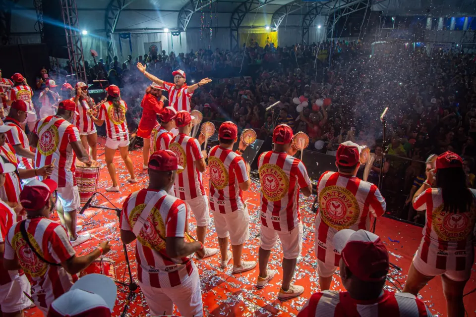 Samba percussion band in red and white performing on stage before a cheering crowd